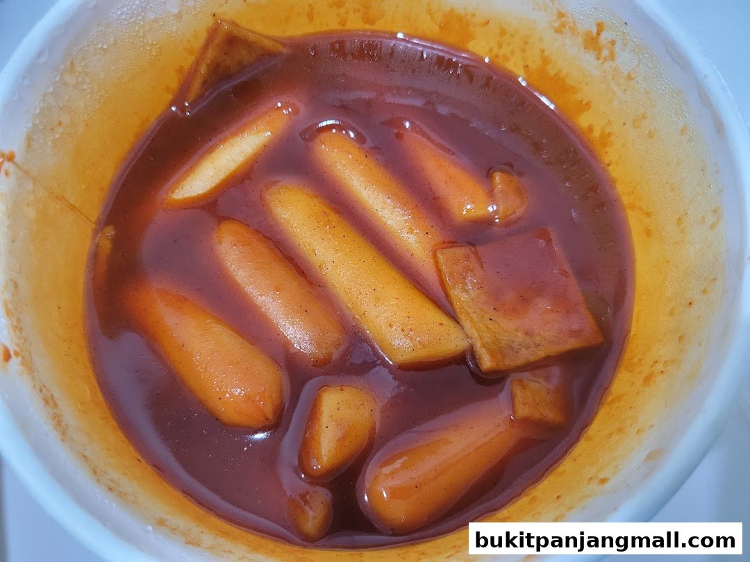 A close-up shot of Korean Tteokbokki in a white bowl with a rich red sauce.