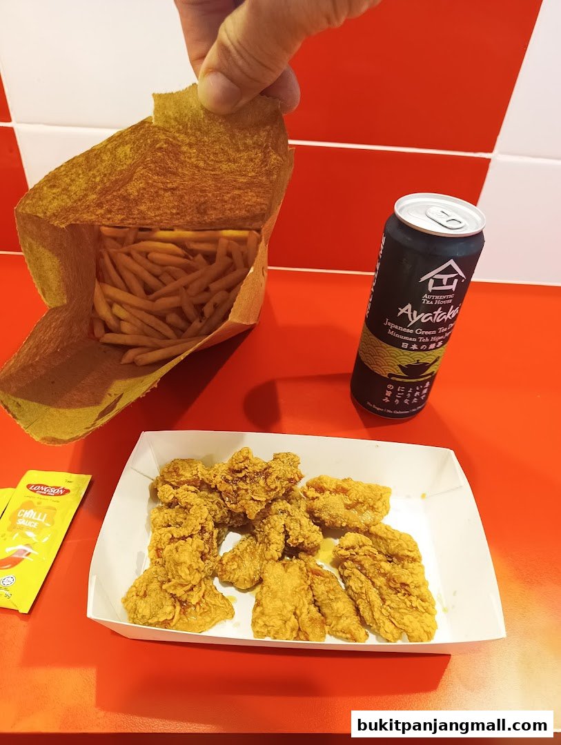 A person holding a paper bag of fries over a tray of Korean fried chicken and a can of Ayataka green tea.
