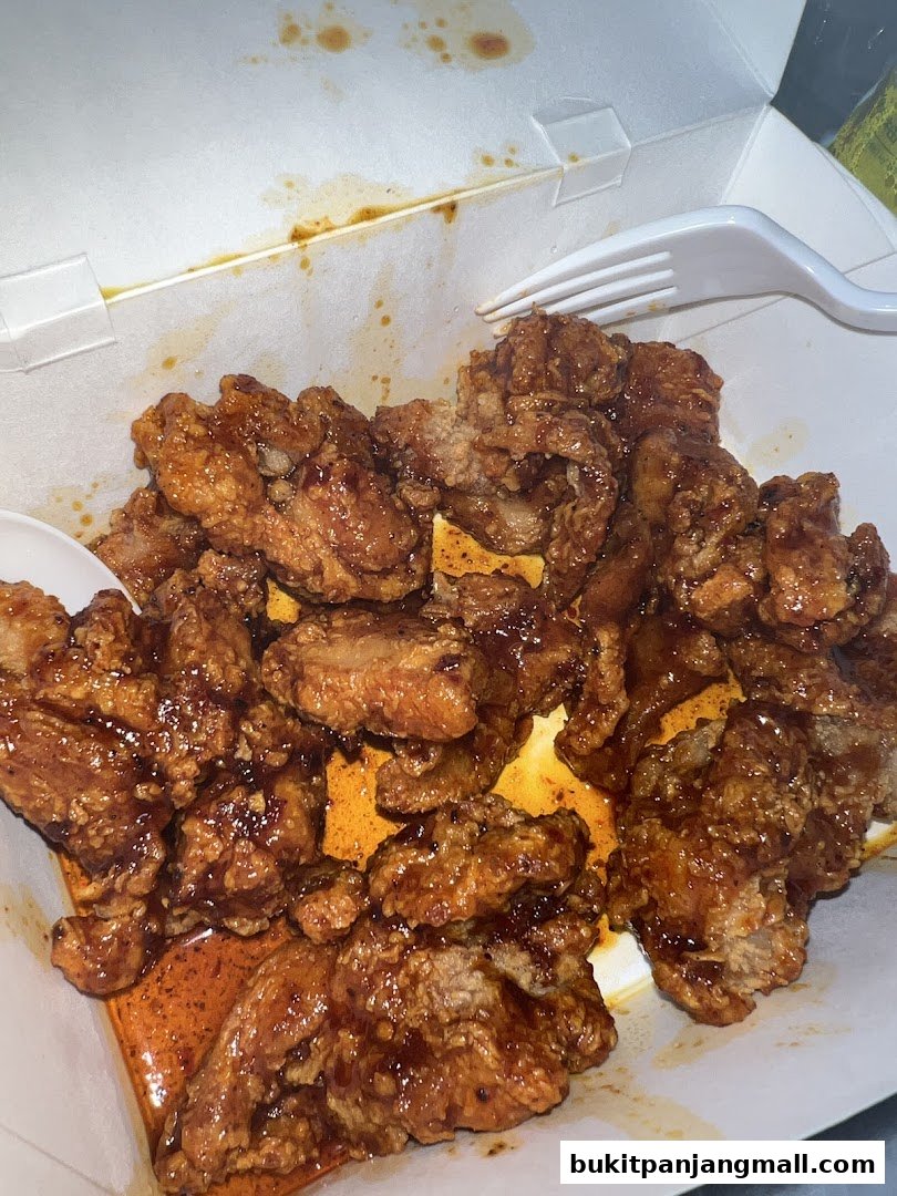 A box of delicious Korean fried chicken with a glossy sauce and a fork.