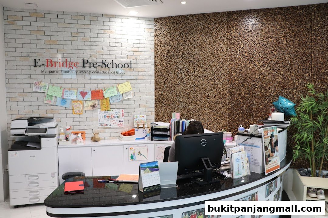 The reception area of E-Bridge Pre-School, featuring a desk with a computer, children's artwork, and a printer.