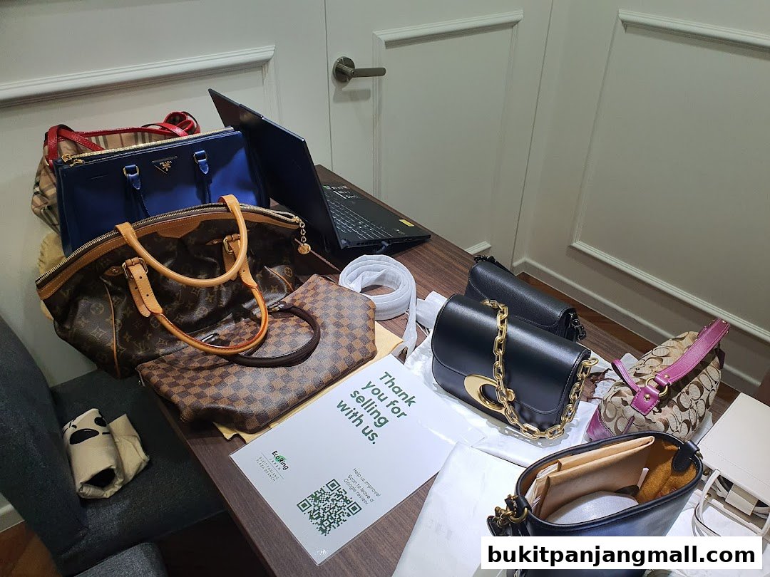 A collection of luxury handbags displayed on a table, with a laptop and a sign.