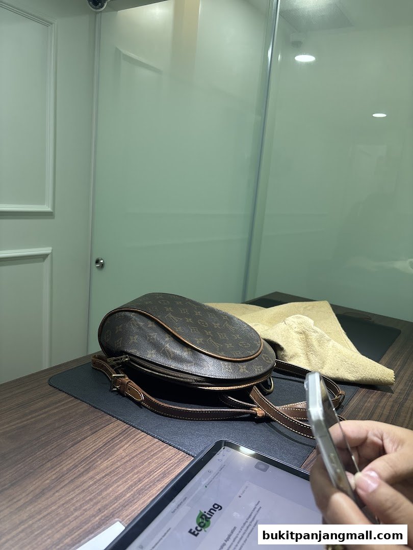 A branded Louis Vuitton bag is displayed on a wooden desk with a tablet and a hand holding a phone.