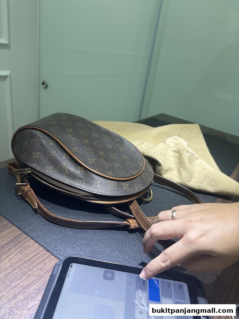 A branded handbag is displayed on a table with a hand interacting with a tablet.