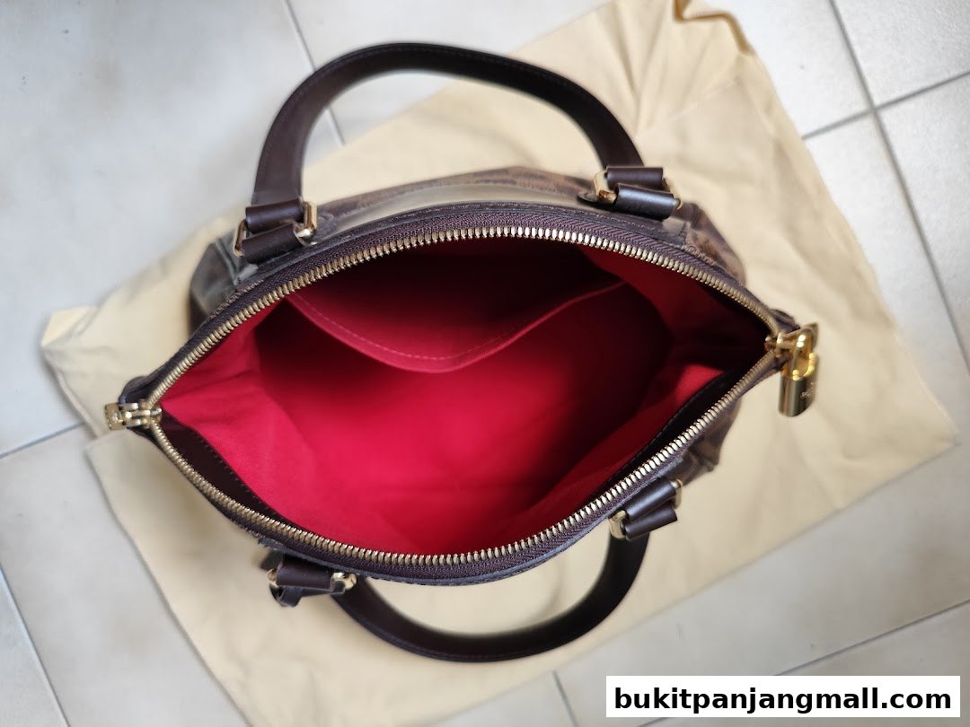 An open designer handbag with a red interior and gold hardware, placed on a dust bag.