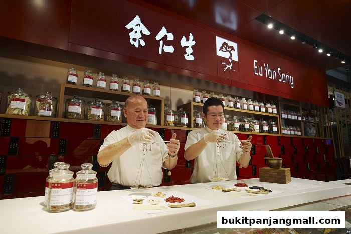 Two men in white coats weigh traditional Chinese medicine ingredients behind a counter.