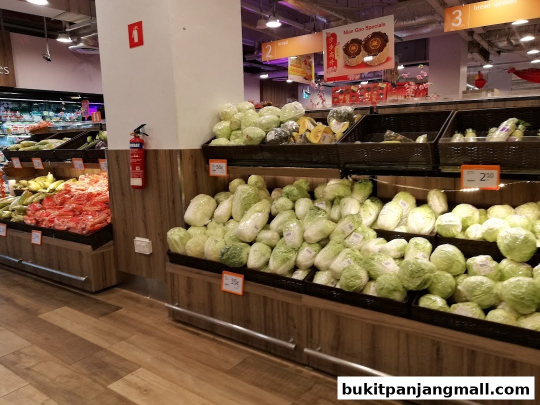 A wide selection of fresh vegetables, including cabbages and other greens, displayed in a supermarket aisle.