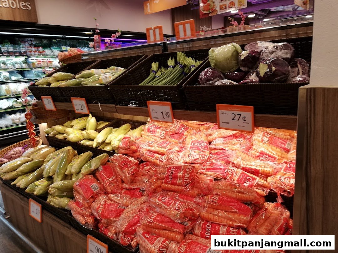A display of fresh vegetables, including corn, carrots, cabbage, and red cabbage, at a grocery store.