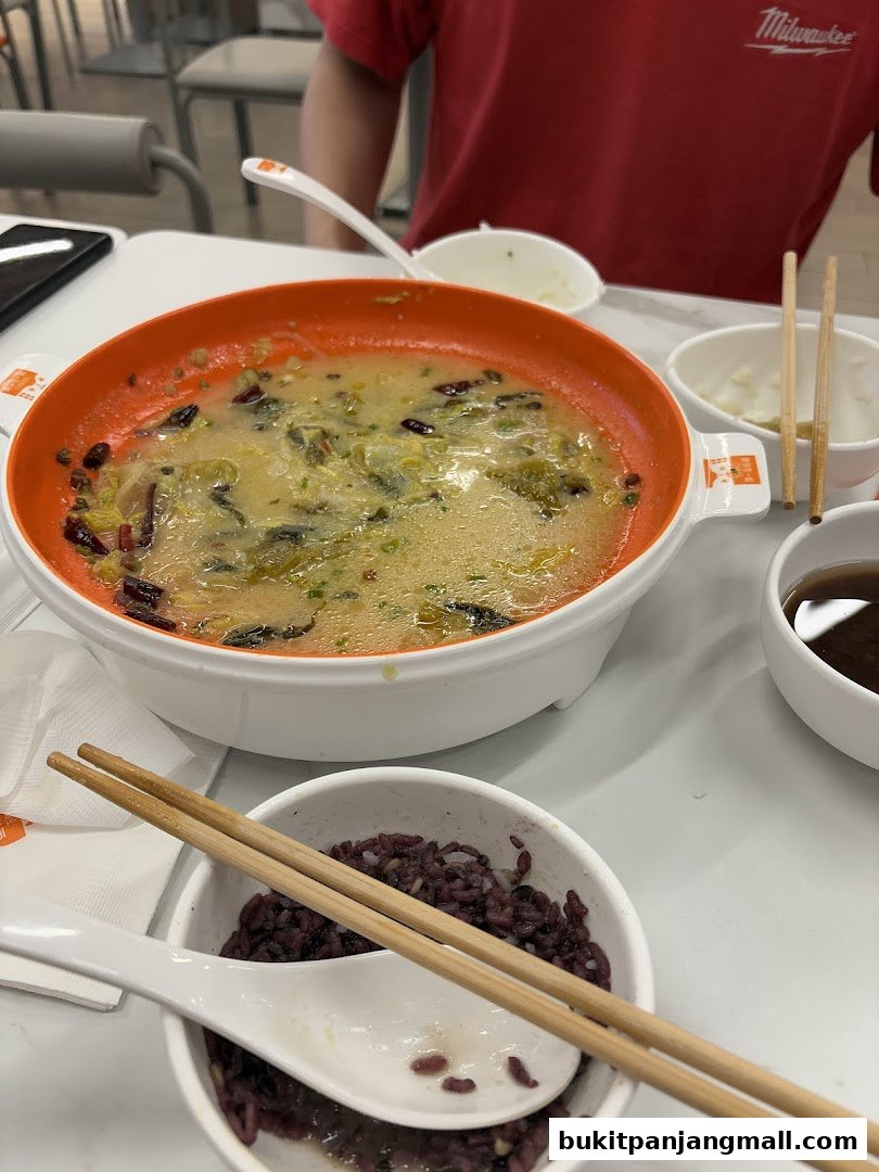 A close-up of a meal with a bowl of soup, rice, and chopsticks.