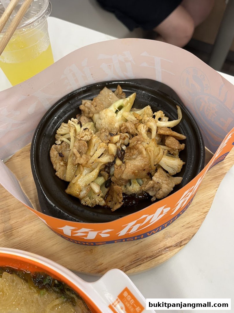 A close-up of a sizzling hot plate dish with meat and cauliflower, served with a drink.