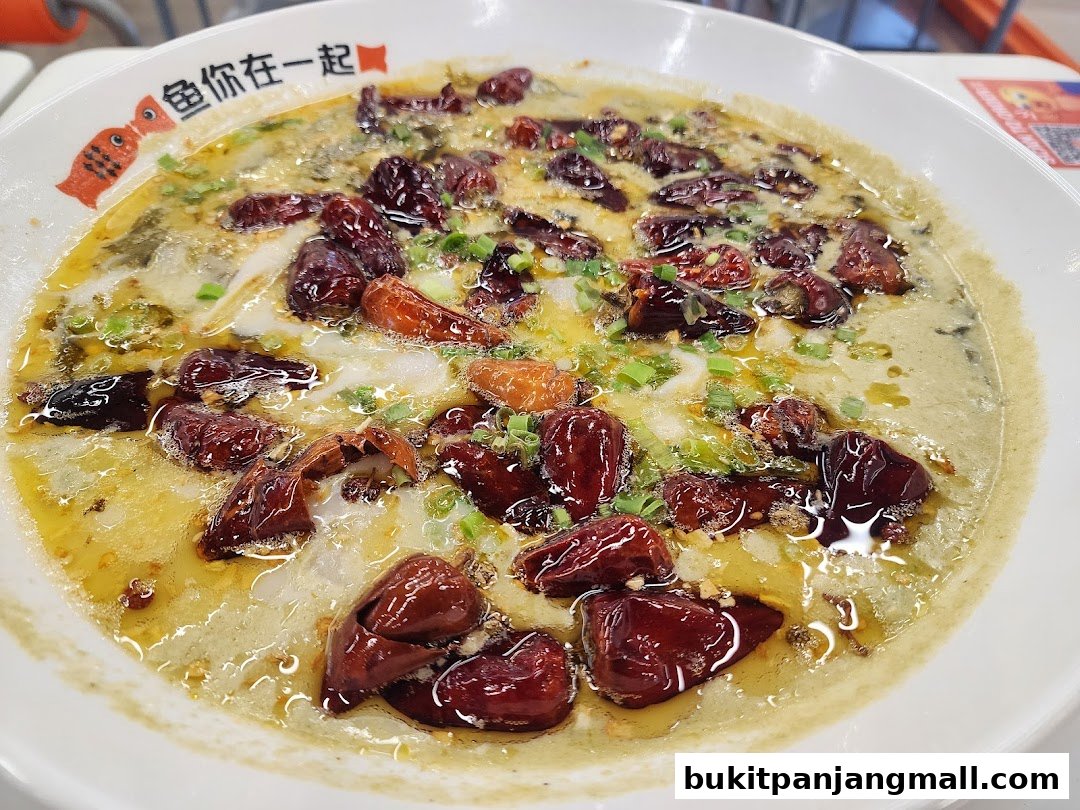A close-up of a bowl of fish soup with dried chilies and scallions.