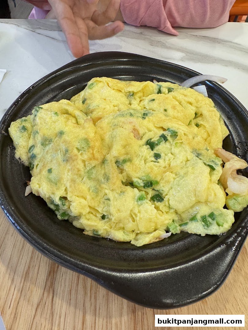 A close-up shot of a fluffy omelet with green onions and shrimp on a black plate.