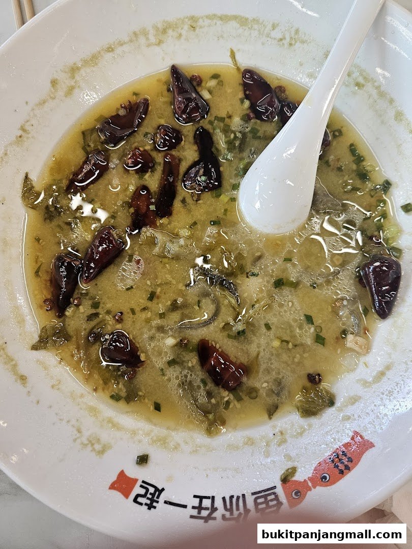 A close-up of a bowl of spicy fish soup with dried chilies and herbs.