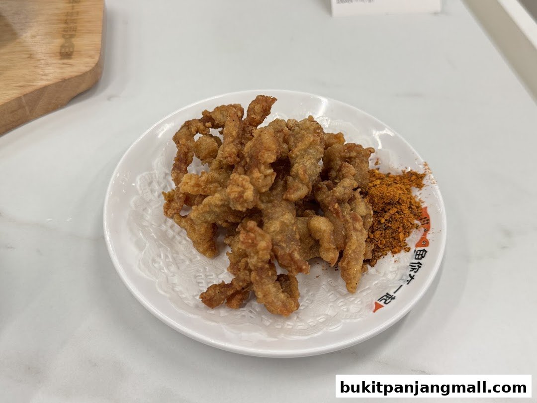 A plate of crispy fried chicken pieces with a side of chili powder.