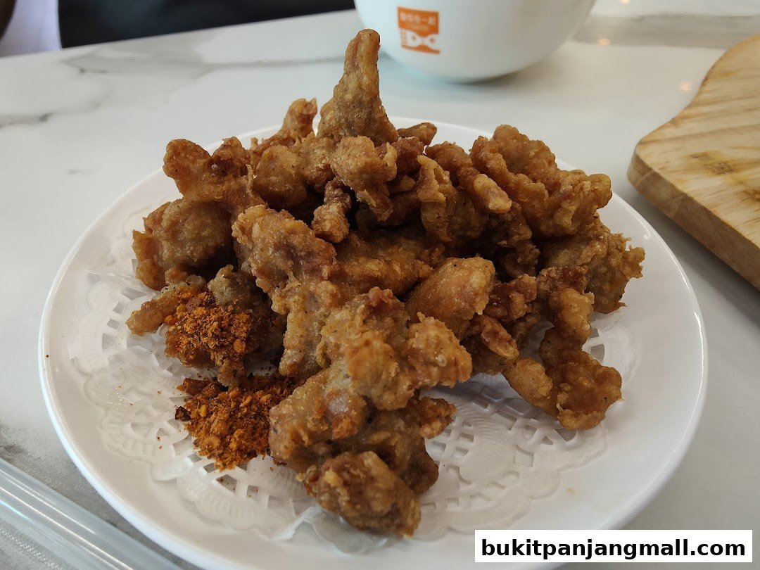 A plate of crispy fried chicken pieces with a side of chili powder.