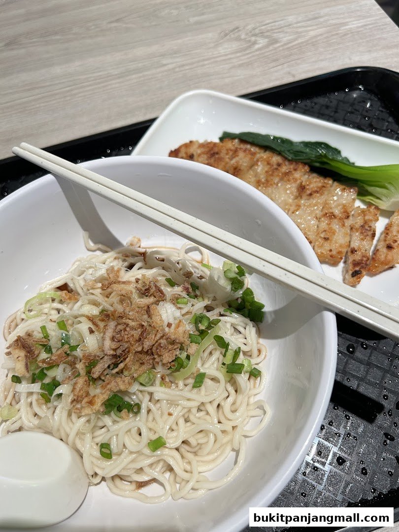 A bowl of noodles with fried shallots and green onions, served with grilled meat and greens.