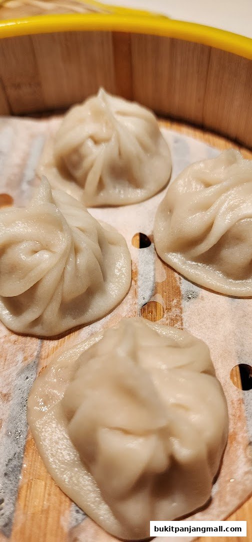 Close-up of four steamed dumplings in a bamboo steamer basket.