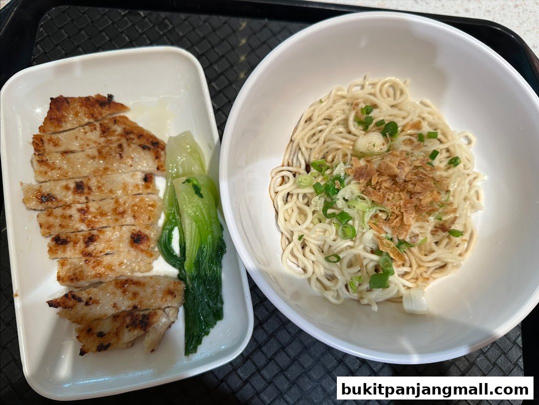 A close-up of a delicious meal featuring grilled pork chops and noodles with green onions.