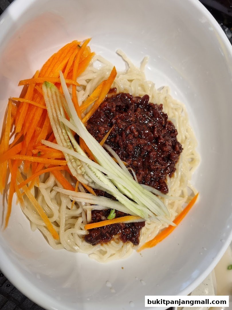 A bowl of noodles topped with minced meat sauce, shredded carrots, and cucumber.