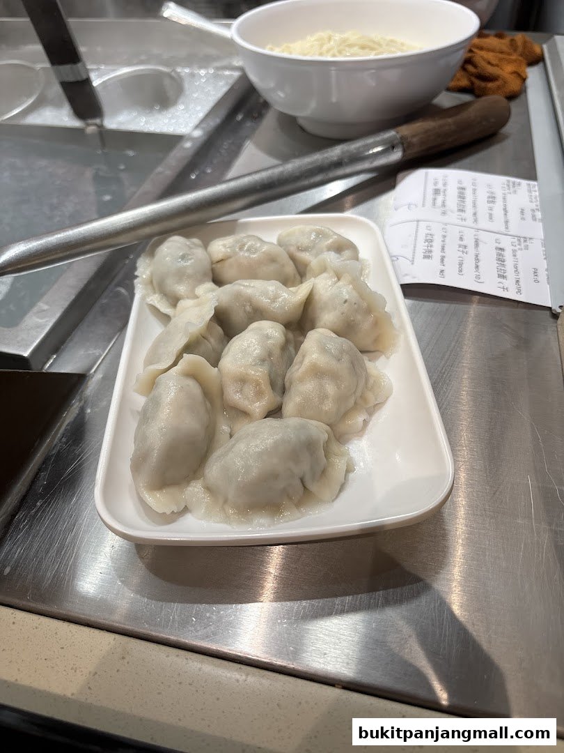 A plate of freshly steamed dumplings sits next to a bowl of noodles.