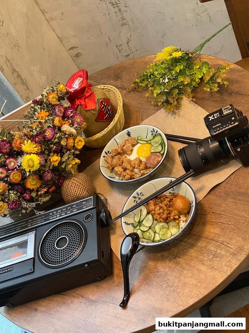 Two bowls of rice with toppings, a vintage radio, dried flowers, and a camera on a wooden table.