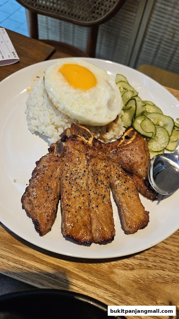 A plate of food with pork chops, rice, a fried egg, and sliced cucumbers.