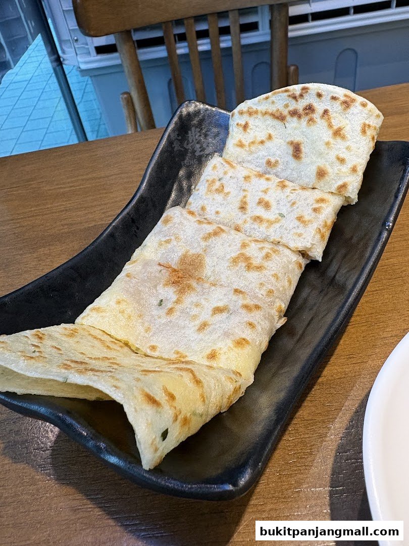 A black plate filled with folded savory crepes on a wooden table.