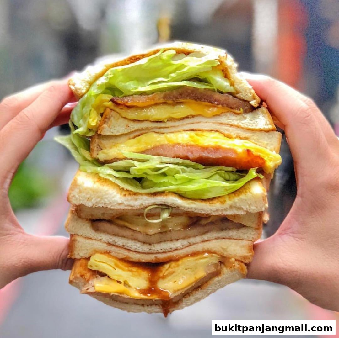 A person holds a tall, stacked sandwich with lettuce, egg, and meat.