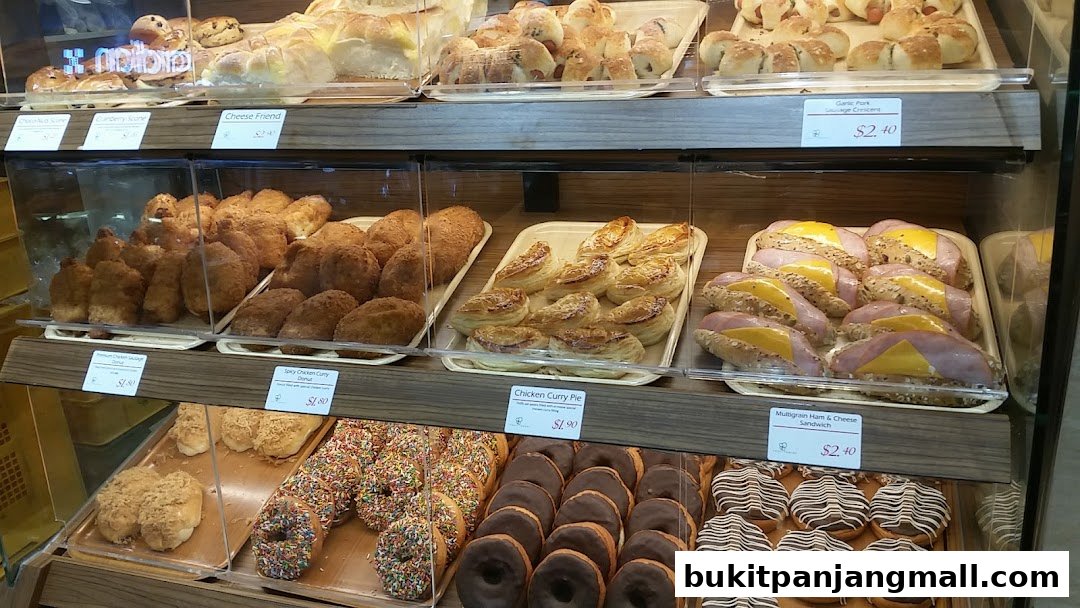 A display case filled with various baked goods including bread, pastries, sandwiches, and donuts.