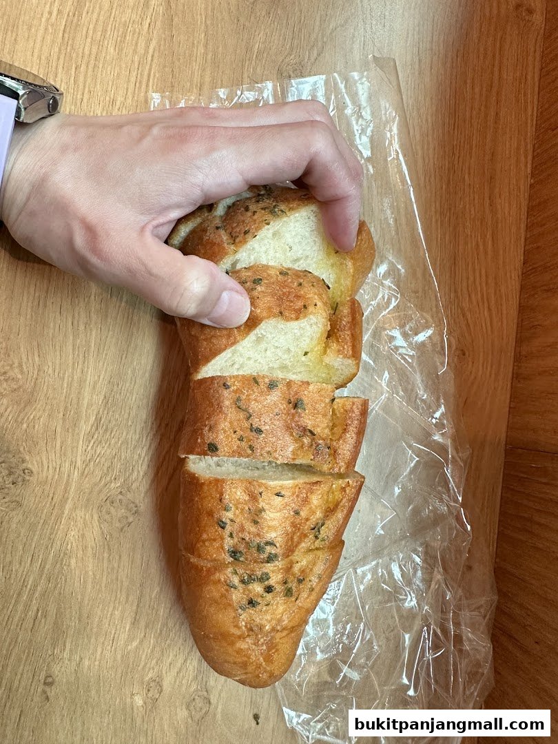 A hand holds sliced garlic bread on a wooden surface.