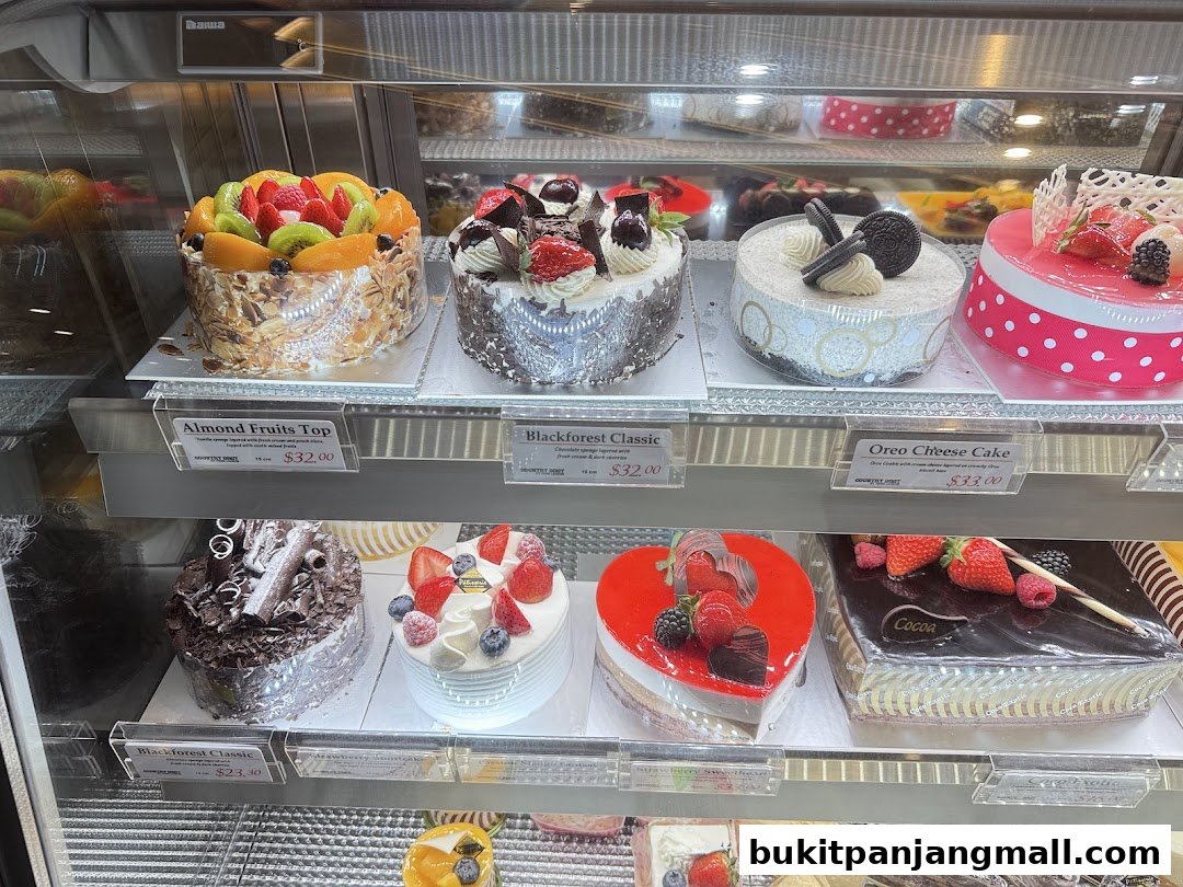 A display case filled with various beautifully decorated cakes, including fruit-topped, chocolate, and cheesecake varieties.