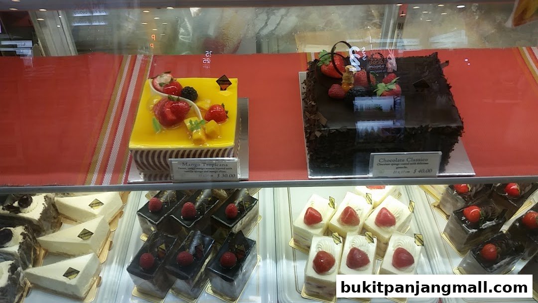 A display case filled with various cakes and pastries, featuring fruit-topped options.