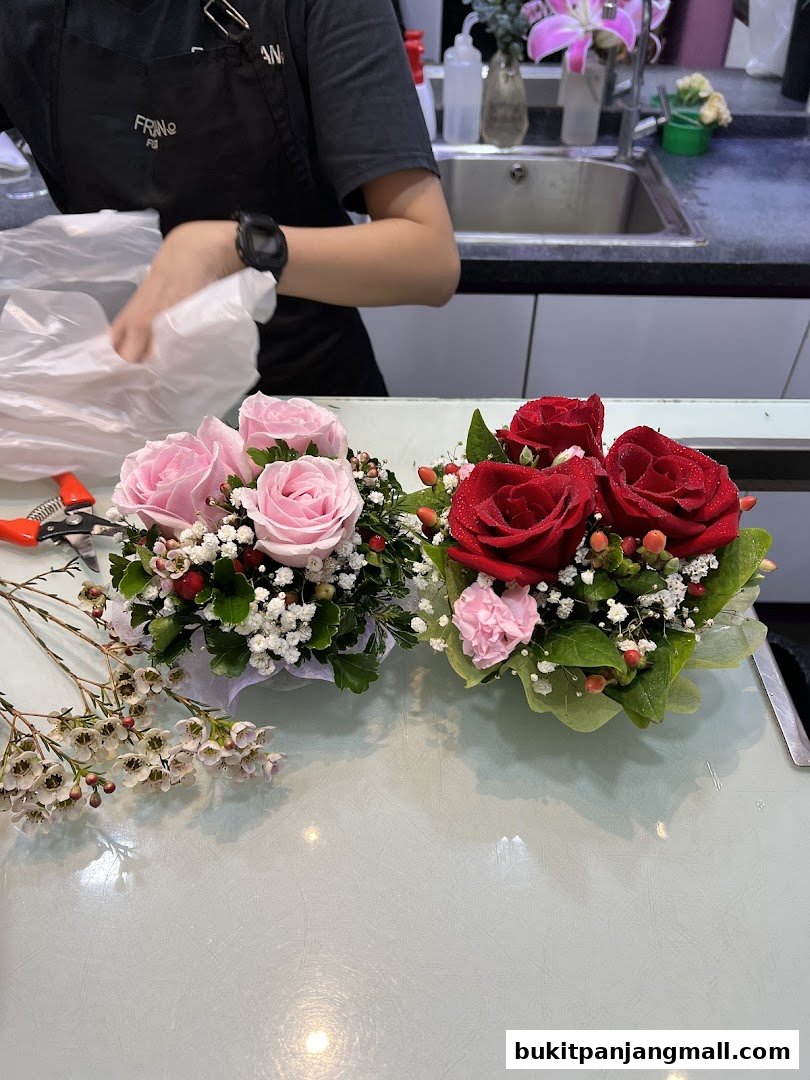 A florist arranging beautiful pink and red rose bouquets with delicate white filler flowers.
