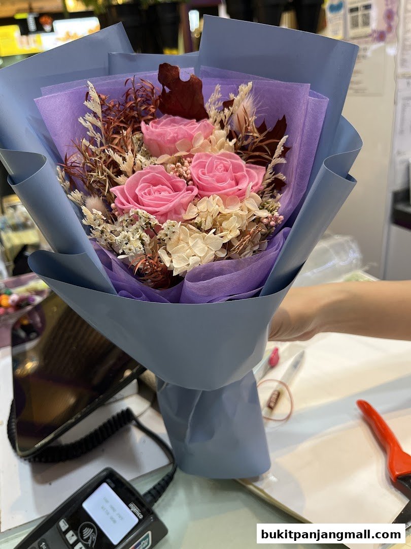 A hand holds a beautiful bouquet of pink preserved roses and dried flowers.