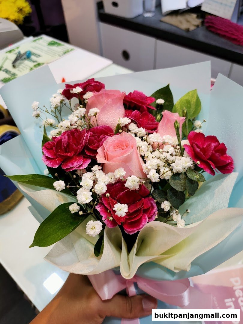 A hand holds a beautiful bouquet of pink roses and dark pink carnations with baby's breath.