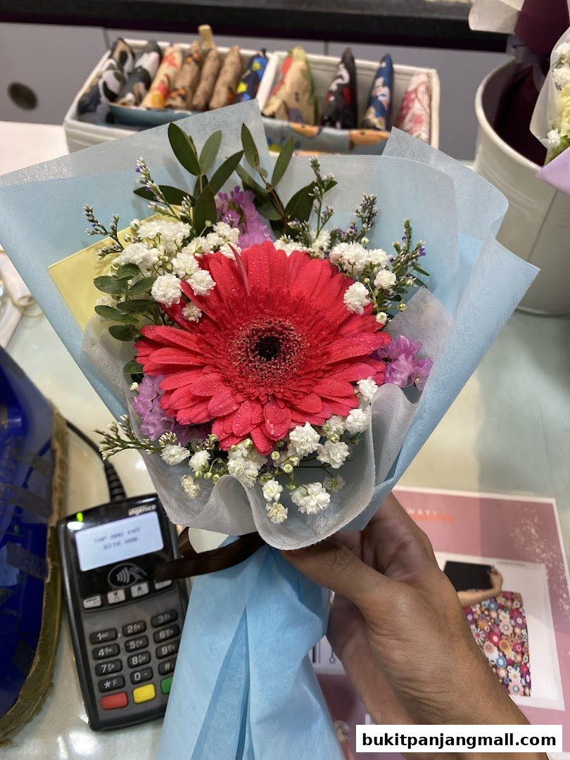 A hand holds a vibrant bouquet of flowers with a payment terminal in the foreground.