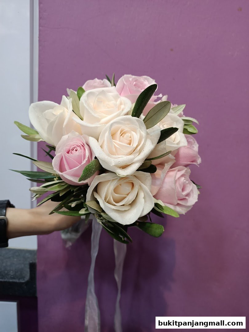 A hand holds a beautiful bouquet of pink and white roses with green leaves.