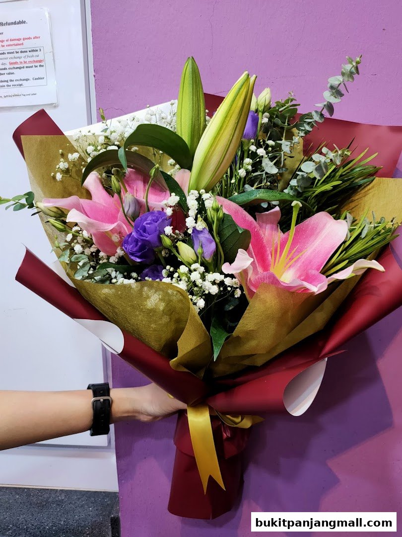 A hand holding a vibrant bouquet of pink lilies, purple lisianthus, and eucalyptus.
