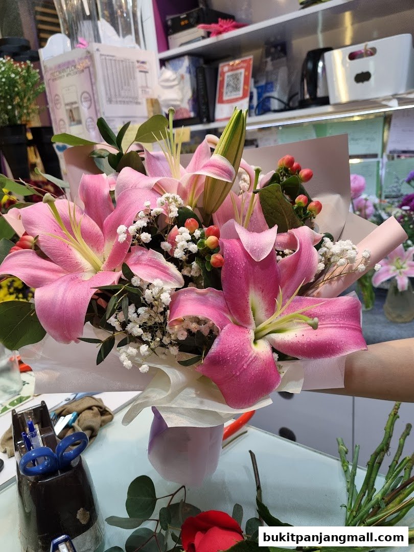 A hand holds a beautiful bouquet of pink lilies and baby's breath.