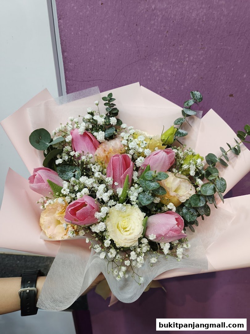 A hand holding a beautiful bouquet of pink tulips, white roses, and baby's breath.