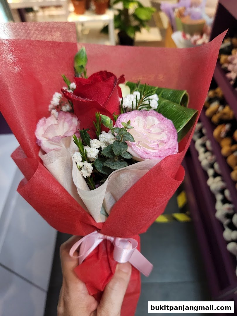 A hand holds a beautifully arranged bouquet of red roses and pink carnations.