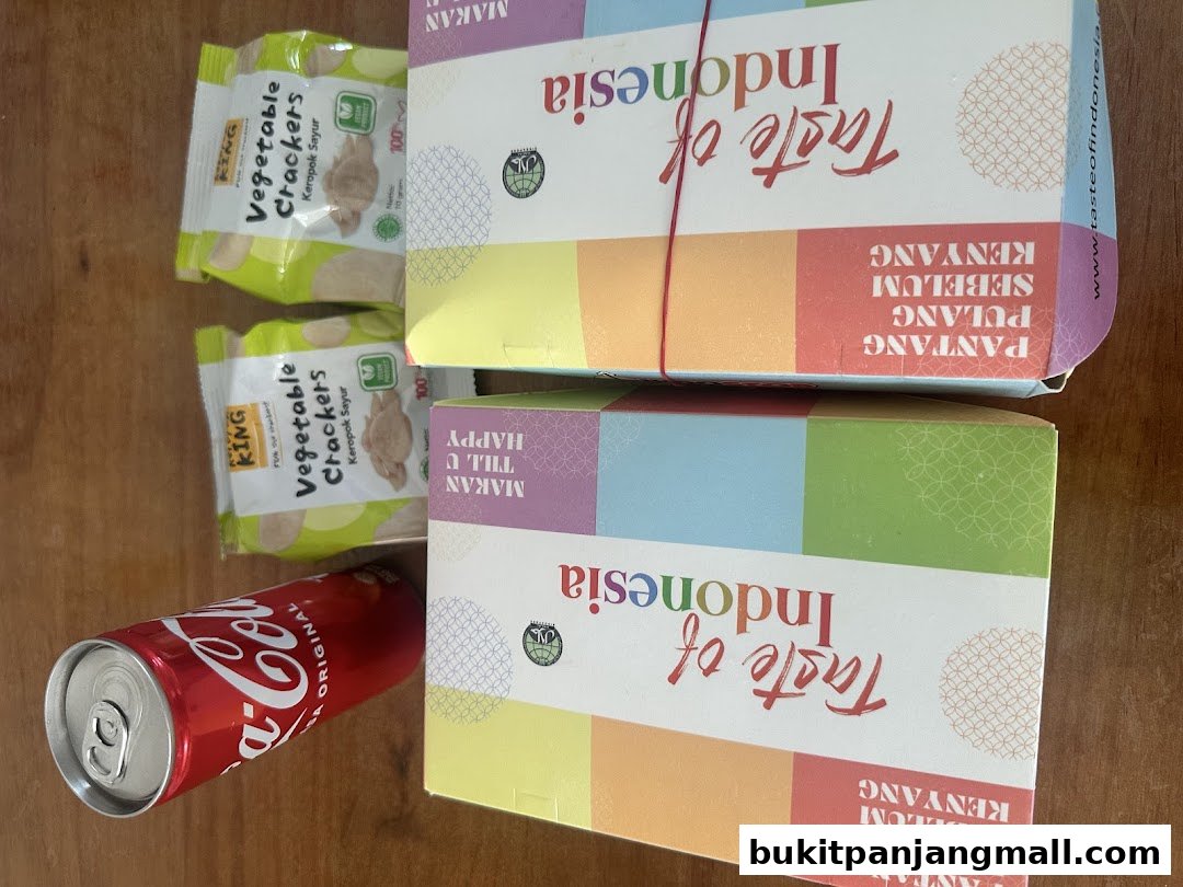 A can of Coca-Cola and two packs of vegetable crackers next to boxes labeled 'Taste of Indonesia'.