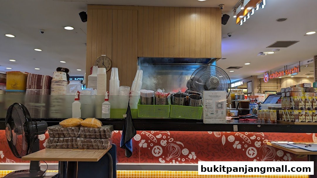 A counter at Gado Grill with food items, fans, and supplies, with Ichiban Sushi visible in the background.