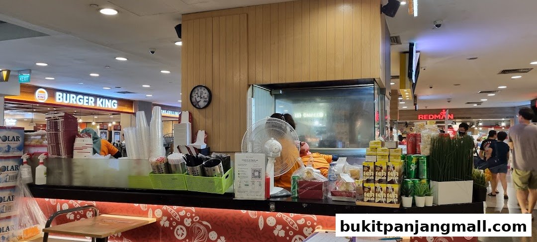 A food stall counter with drinks, snacks, and utensils, with Burger King and Redman stores in the background.