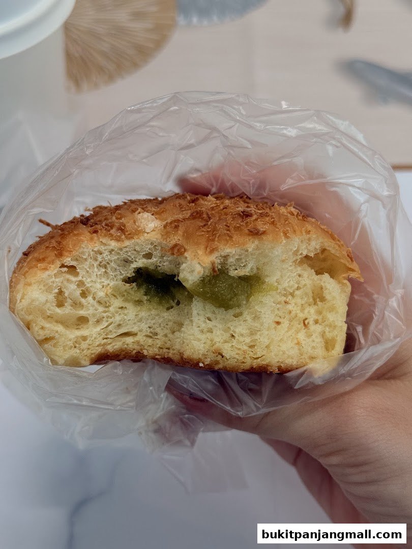 A close-up of a Japanese sweet bun with a green filling, held in a plastic bag.