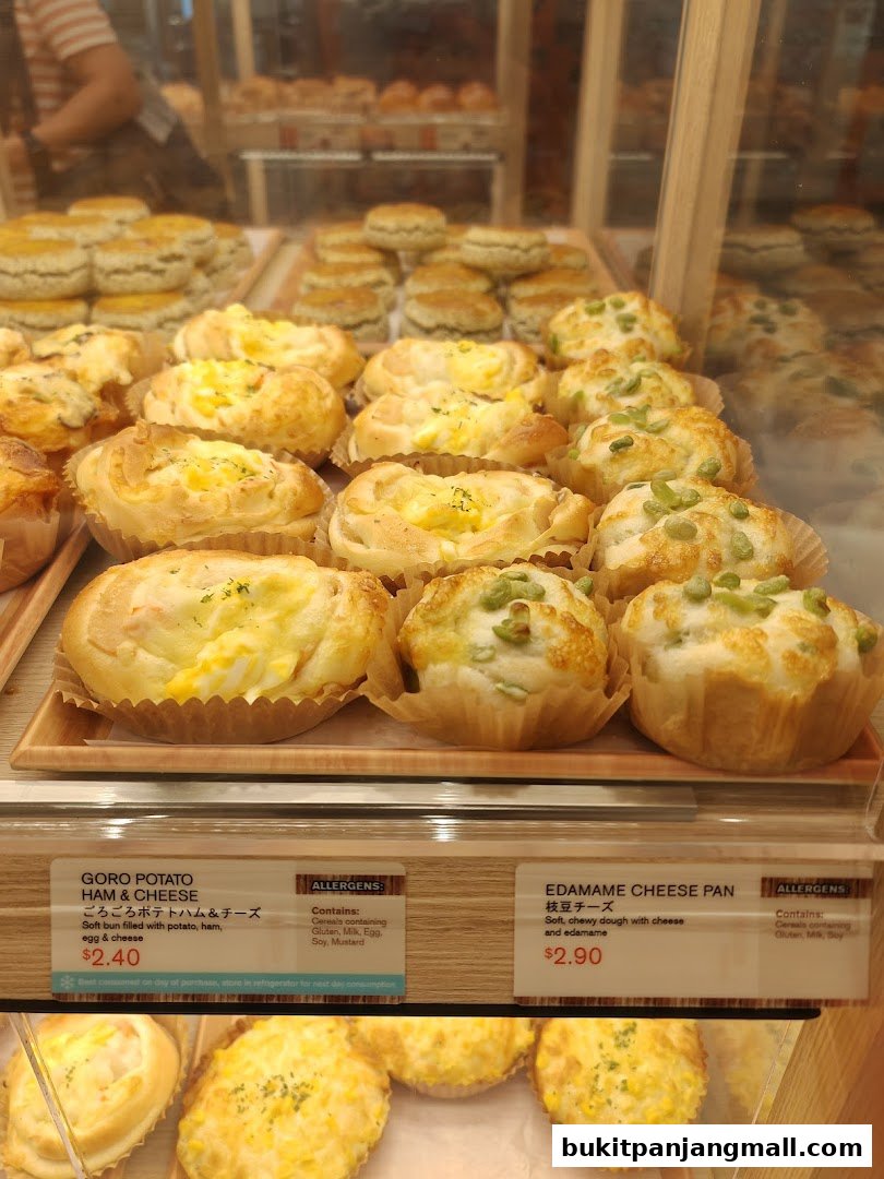 A display of freshly baked Japanese buns with various fillings, including potato, ham, cheese, and edamame.