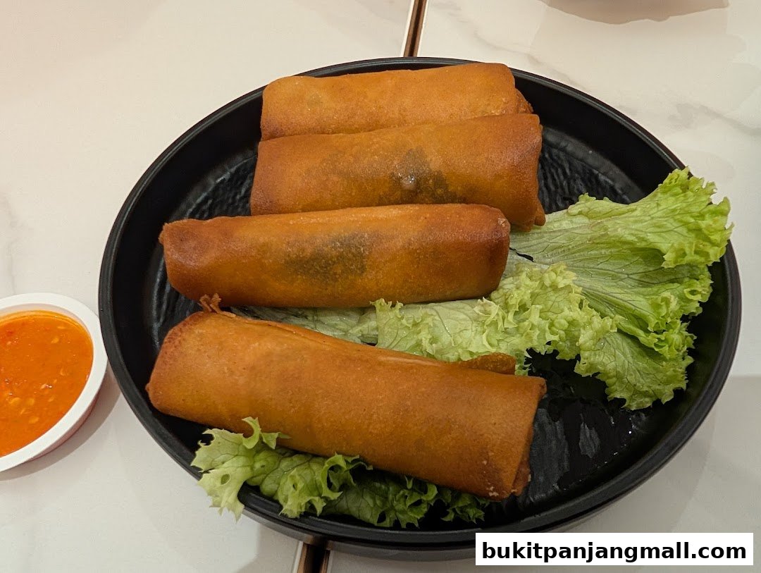A plate of golden-brown spring rolls served with a side of chili sauce and lettuce.