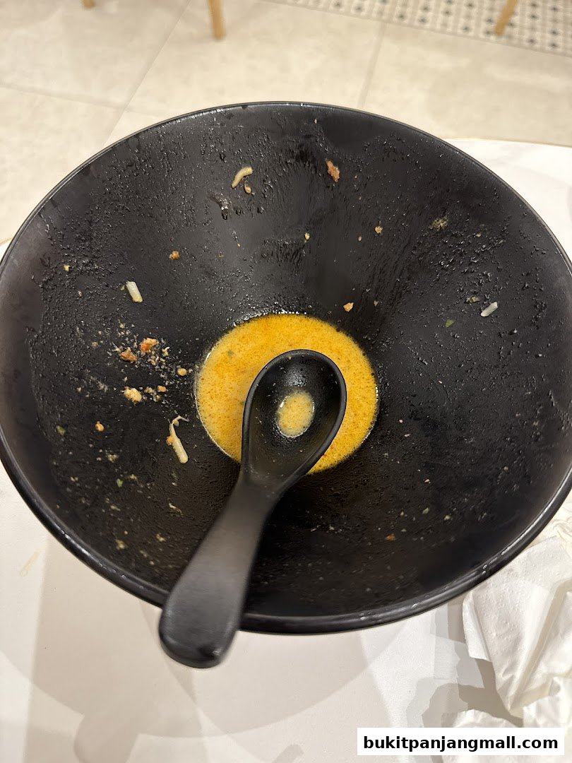 A close-up of an empty black bowl with a spoon and leftover broth.