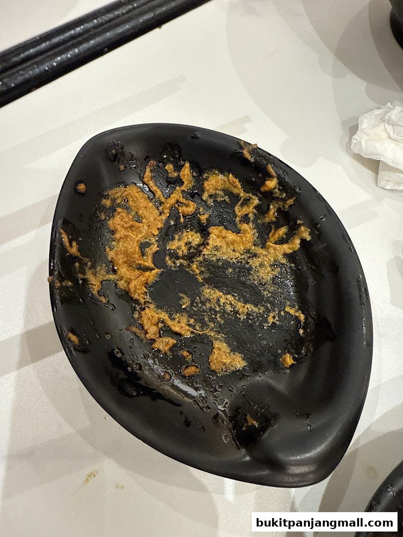 A black plate with leftover food residue and chopsticks on a white table.