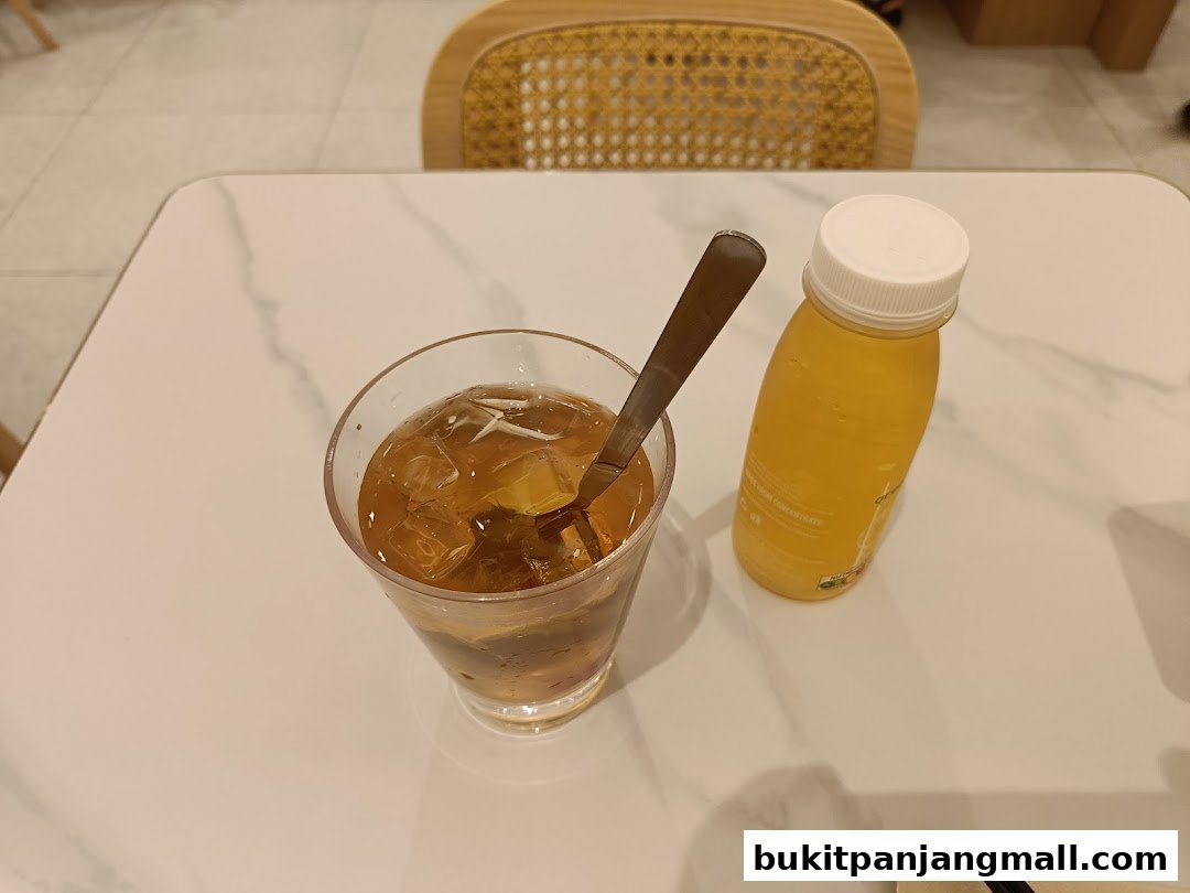 A glass of iced tea and a bottle of orange juice on a white marble table.