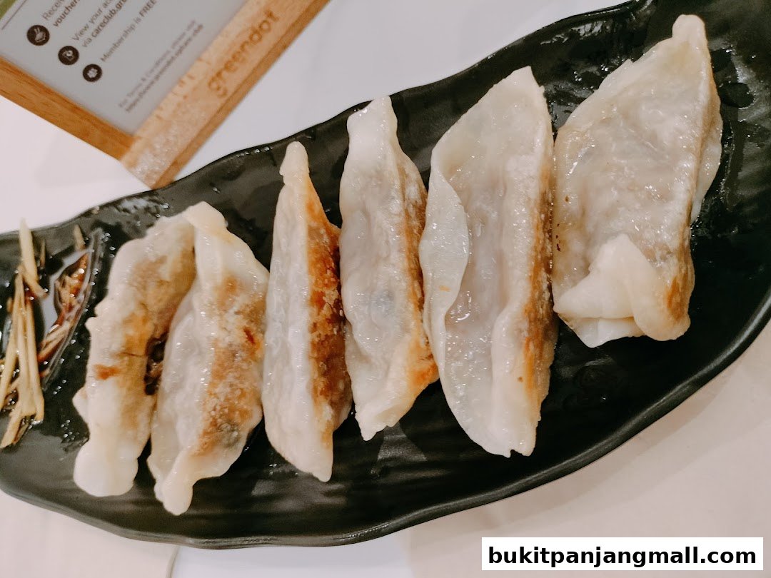 A plate of pan-fried dumplings with ginger slices and dipping sauce.